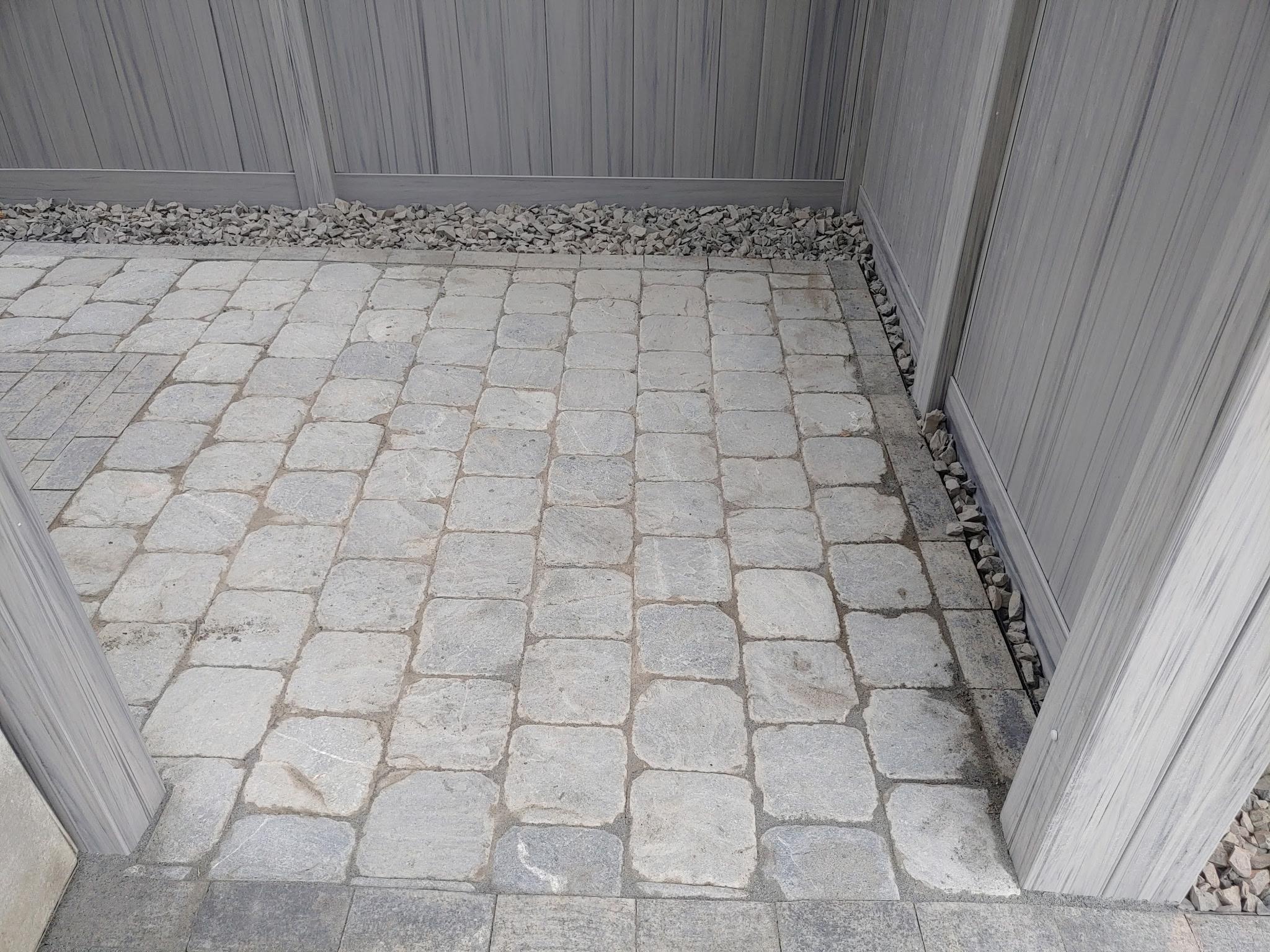 Completed cobblestone paver surface between grey vinyl fence sections